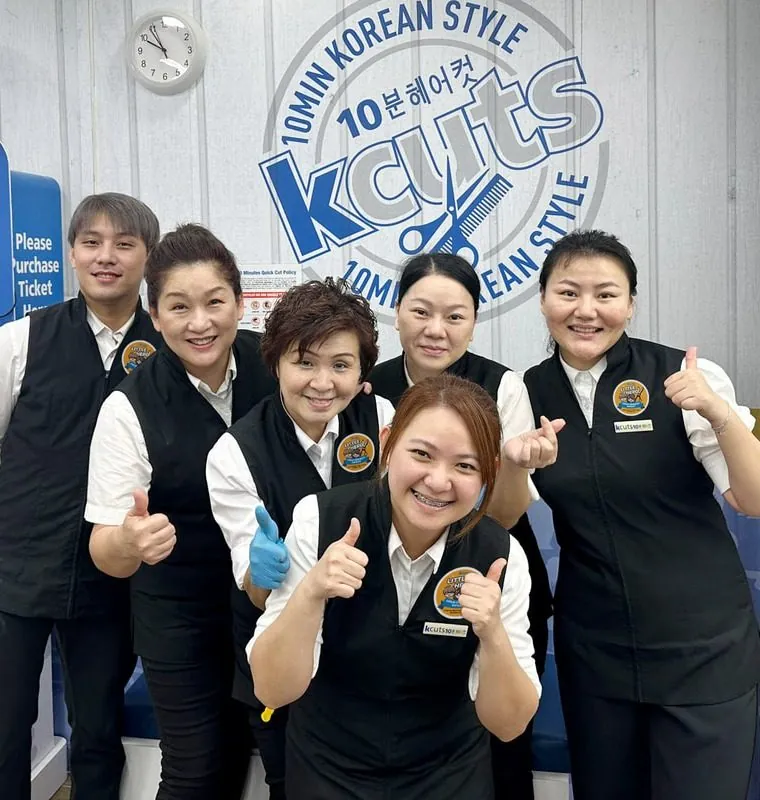 The kcuts stylist team smiling in front of the 10-minute Korean style branded wall